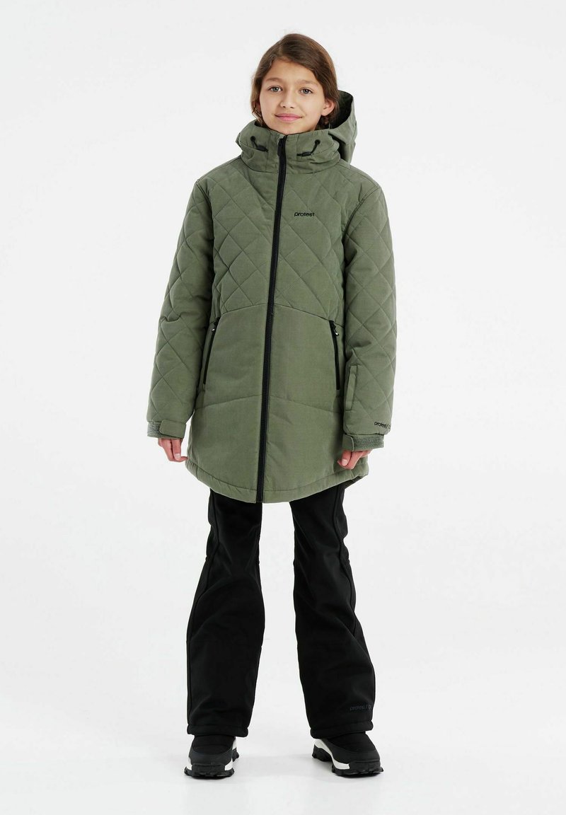 Giacca da esterno verde trapuntata con cappuccio, dotata di zip frontale, tasche laterali e una vestibilità comoda. Abbinata a pantaloni neri e stivali.