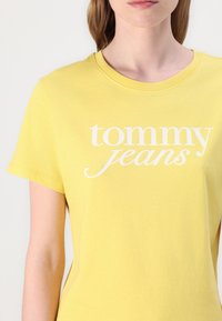 Kollane lühikeste varrukatega T-särk, mis on valmistatud puuvillast. Rinnal on valge "tommy jeans" tekstilogo, ümar kaelus ja lõdvestatud istuvus.