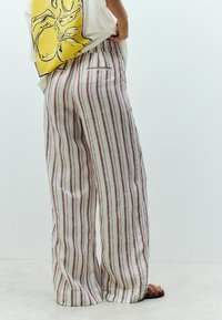 Pantaloni in lino a righe con una vestibilità rilassata, caratterizzati da righe verticali rosse e bianche, una vita elasticizzata e una tasca posteriore singola.