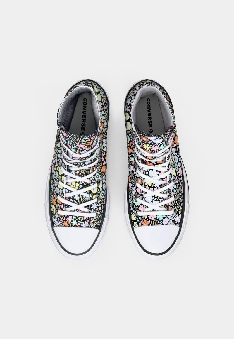 Baskets basses en toile sur fond noir, ornées de motifs floraux multicolores, avec des lacets blancs et des embouts en caoutchouc blancs.
