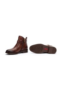 Brown leather ankle boots with a side zipper, diagonal strap detailing, and a low block heel. Textured rubber sole with grip patterns.