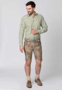 Groen en wit geblokt overhemd met lange mouwen, gecombineerd met bruine leren lederhosen, voorzien van bloemmotieven en een riem met een metalen gesp.