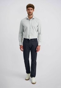 Hellgrünes Hemd mit Knopfleiste, dunkelblaue Hose und weiße Sneaker. Das Hemd hat ein dezentes Muster; die Hose verfügt über Eingrifftaschen und einen klassischen Schnitt.
