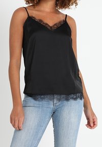 Camisole noire à fines bretelles, avec un décolleté en V et une bordure en dentelle le long de l'ourlet et du décolleté. Tissu lisse, effet satin.