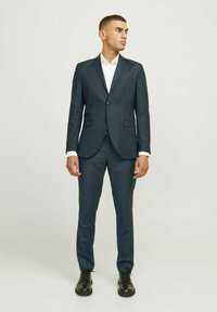 Mørkegrøn habit med en tætsiddende design, enkeltknappet jakke, notch-lapel og matchende bukser. Hvid skjorte og sorte sko fuldender udseendet.