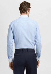 Svetlo modra srajca s črtami, klasičnim ovratnikom, dolgimi rokavi in belimi manšetami, kombinirana s temnimi hlačami. Gladek material s prilagojeno prileganjem.