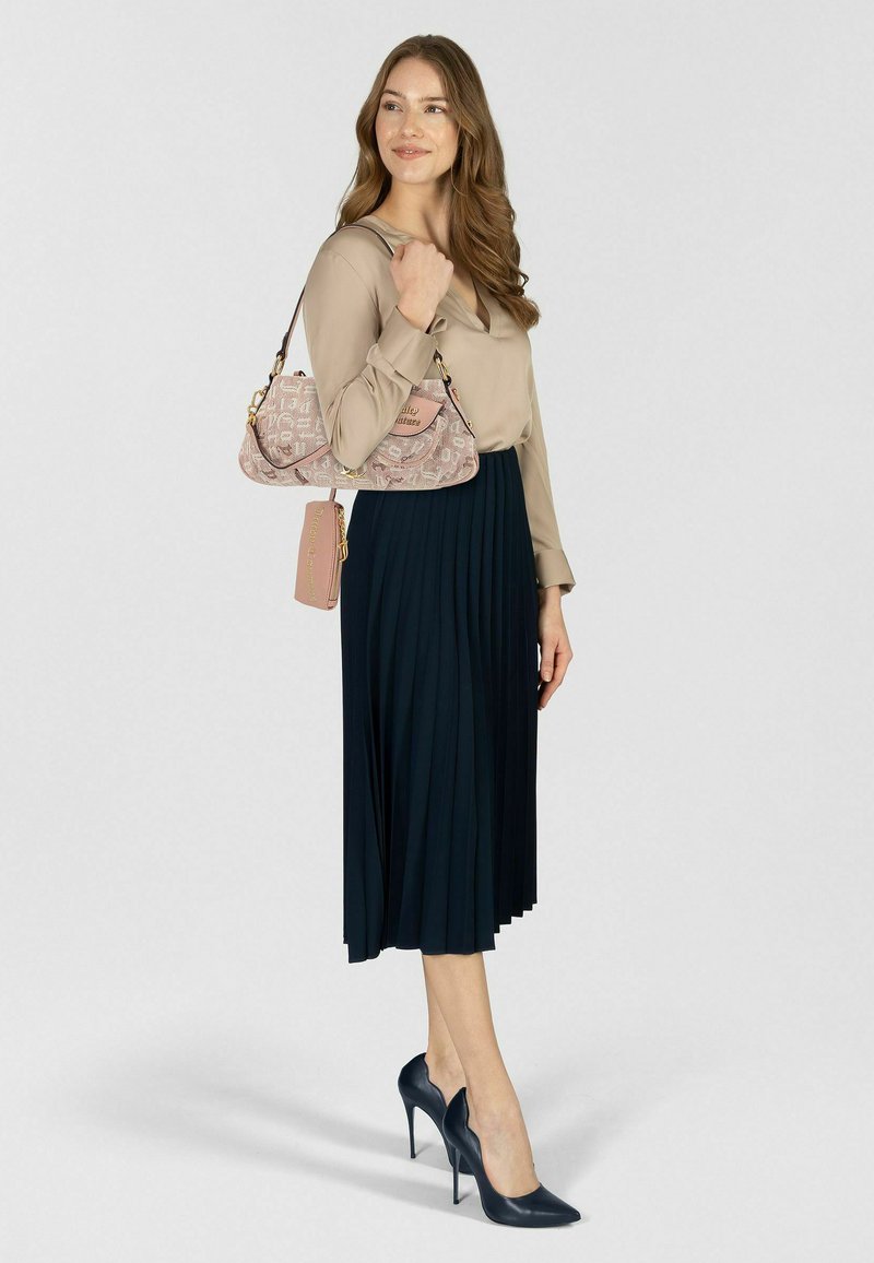 Blusa beige a maniche lunghe, gonna plissettata blu navy e décolleté blu navy. Borsa rosa con motivo, con dettagli dorati e targhetta con il nome.