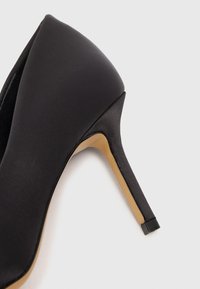Décolleté nera in satin con punta affusolata e tacco stiletto elegante. Presenta una superficie liscia e una suola beige in contrasto. Accentuata da una finitura lucida.