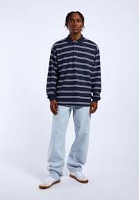 Polo de rayas azul marino y blanco de manga larga con cuello, combinado con jeans sueltos de color azul claro y zapatillas blancas con suela de goma.