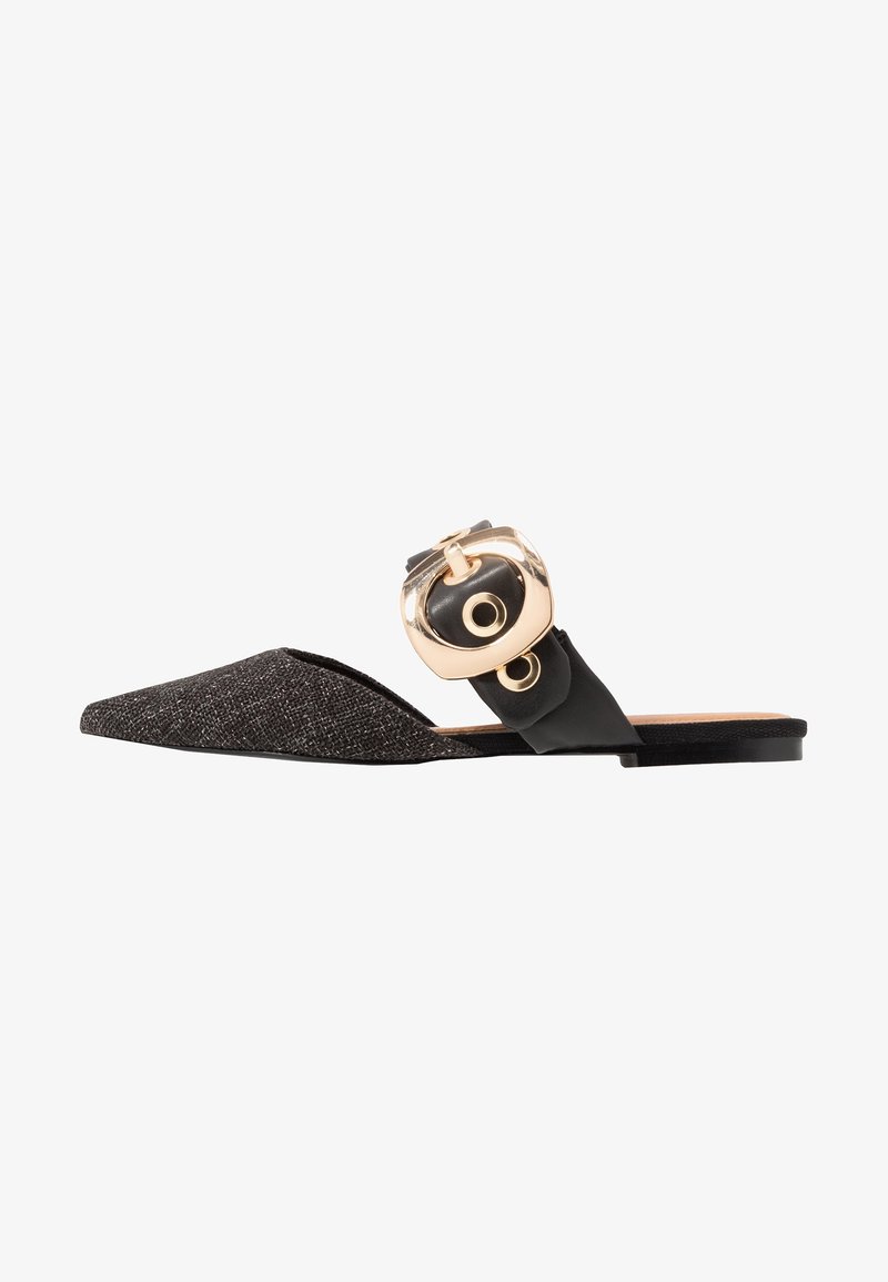 Chaussure plate à enfiler noire et argentée avec un bout pointu, présentant un dessus texturé et une boucle d'accent dorée proéminente sur une sangle noire.