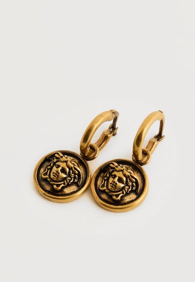 Κρίκοι σκουλαρίκια σε χρυσό τόνο με στρογγυλά κρεμαστά διακοσμημένα με ανάγλυφη κεφαλή της Μέδουσας σε απλό λευκό φόντο.