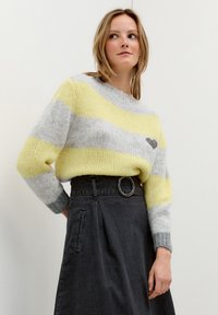 Gestreifter Pullover aus gelbem, grauem und weißem Garn, mit rundem Ausschnitt und lockerem Sitz, kombiniert mit einem schwarz hochtaillierten Rock mit Gürtel.