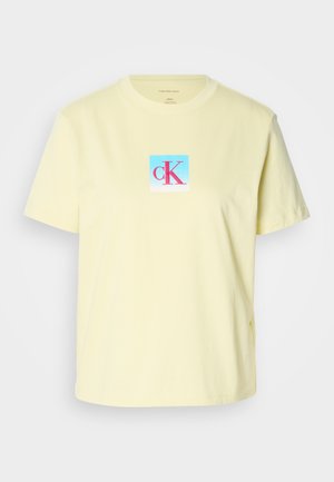 Gaiši dzeltena kokvilnas T-kreklu ar īsām piedurknēm, kurā centrā ir kvadrātveida logo ar rozā un zilā gradienta "cK" dizainu.