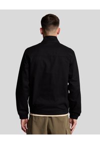 Svart jacka med hög krage, elastiska ärmar och avspänd passform. Tillverkad av slätt tyg. Vy bakifrån som visar enkla design detaljer.