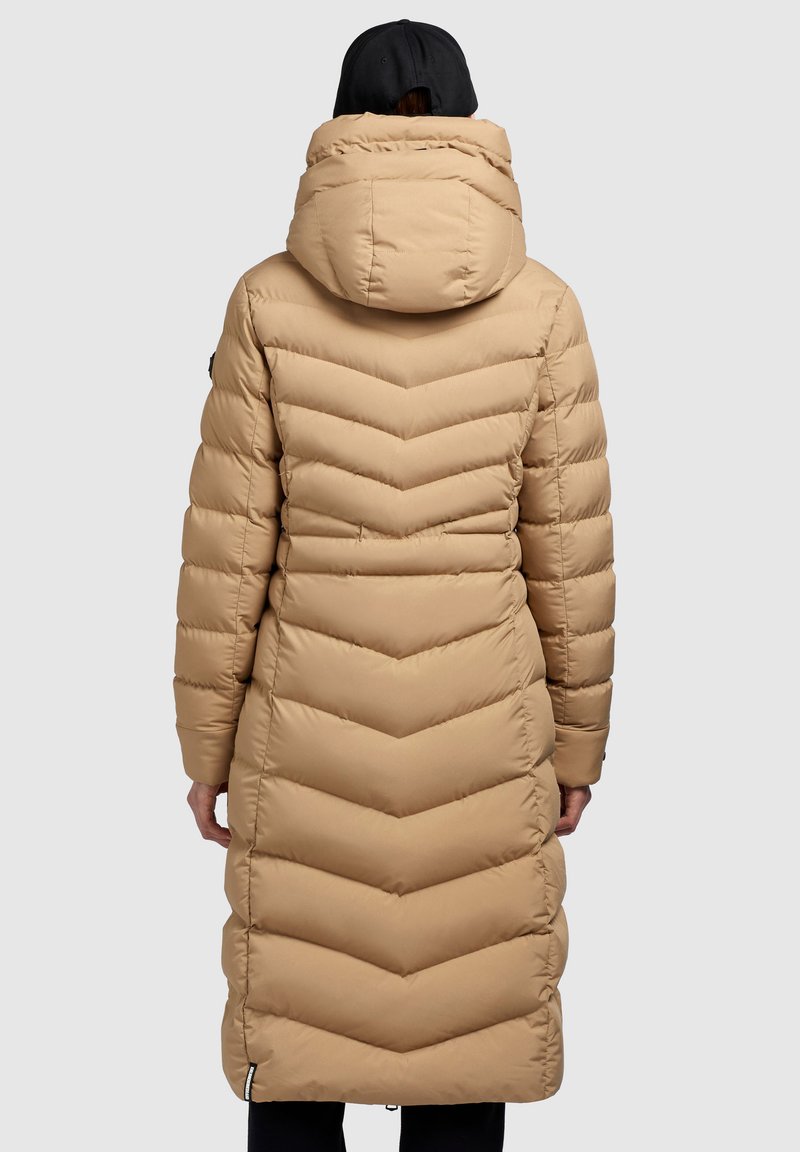 Beige langer Daunenmantel mit einem Zickzack-Steppmuster, abnehmbarer Kapuze und seitlichen Taschen, der mit einer leicht glänzenden, glatten Stoffoberfläche ausgestattet ist.