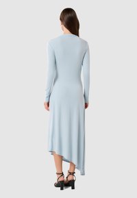 Long-sleeve, light blue dress with a flowy asymmetrical hem, made of soft fabric, paired with black strappy high-heeled sandals.