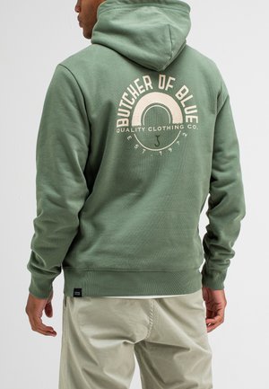 Grüne Baumwoll-Hoodie mit einem grafischen Druck auf der Rückseite, der den Text "BUTCHER OF BLUE" und "QUALITY CLOTHING CO." in Creme zeigt. Lässiges Design.