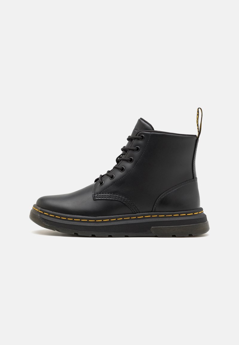 Bottine en cuir noir avec lacets à l'avant, surpiqûres jaunes autour de la semelle, languette à l'arrière et semelle épaisse en caoutchouc noir.