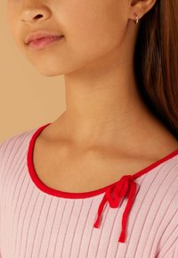 Hellrosa geripptes Oberteil mit einem roten, abgerundeten Ausschnitt und einer gebundenen Akzentuierung an der Schulter. Glatte Textur mit dezenten vertikalen Linien.