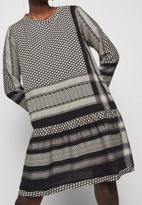 Schwarz-weiß gemustertes Kleid mit langen Ärmeln, rundem Ausschnitt und gestuftem Saum. Es zeichnet sich durch geometrische und gestreifte Designs in verschiedenen Texturen aus.