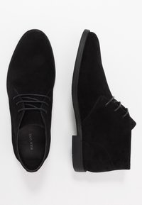 Bottes noires en daim à la cheville avec une finition lisse, un bout rond et de fins lacets. Présente une semelle en caoutchouc noir et des détails de couture minimaux.