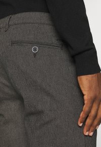 Wollen broek met een gemêleerde, donkergrijze stof, voorzien van een achterzak met knoopdetail, gecombineerd met een zwart trui.