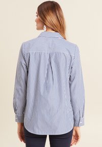 Chemise à rayures bleu et blanc, avec un pli au dos, col et manches longues avec poignets boutonnés. Tissu en coton lisse.