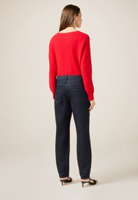Suéter rojo de manga larga combinado con jeans azul oscuro. El suéter tiene un escote amplio; los jeans cuentan con bolsillos en la parte trasera y una cintura ajustada.
