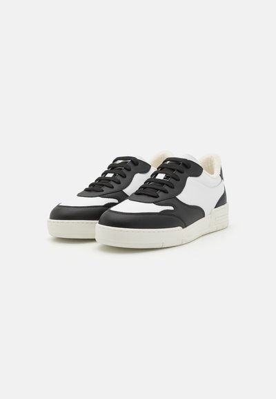 Black and white leather sneakers with textured accents, flat laces, padded collar, and a white rubber sole.