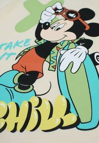 Mickey Mouse dans une tenue colorée avec une veste verte à motifs, un short rouge et des chaussures aqua surdimensionnées, tenant des lunettes de soleil. Le texte indique "PRENDS ÇA COOL".