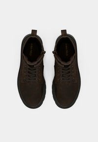 Brūnas zīda zamšādas mežģīņu zābaki ar apaļu purngalu, polsterētu apkakli, šūtiem akcentiem un raupju gumijas zoli. Zīmola nosaukums redzams iekšpusē.