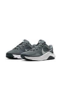 Para szarych siateczkowych butów sportowych z czarnymi i białymi podeszwami oraz srebrnymi logo w kształcie „swoosh”, wyeksponowanych obok siebie na białym tle.