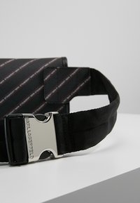 Borsa a cintura in tessuto nero con strisce diagonali rosse e bianche, dotata di un dispositivo di chiusura in metallo argentato con incisione "KARL LAGERFELD".