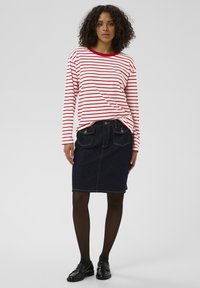 Punaste ja valgete triipudega pikkade varrukatega särk ümmarguse kaelusega, sobitatud tumeda teksapliiatsseelikuga ja mustade loafers-kingadega.