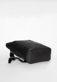 Black rectangular backpack with smooth bottom panel, adjustable straps, and roll-top closure lying on a white surface.