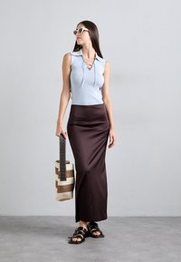 Top fără mâneci, de culoare albastru deschis, cu un gât cu șnur, asortat cu o fustă maxi din satin de culoare maro închis. Modelul ține o geantă țesută în dungi și poartă sandale negre.