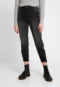High-waisted black denim jeans featuring a tapered leg, frayed hems, and subtle fading, paired with black lace-up ankle boots.
