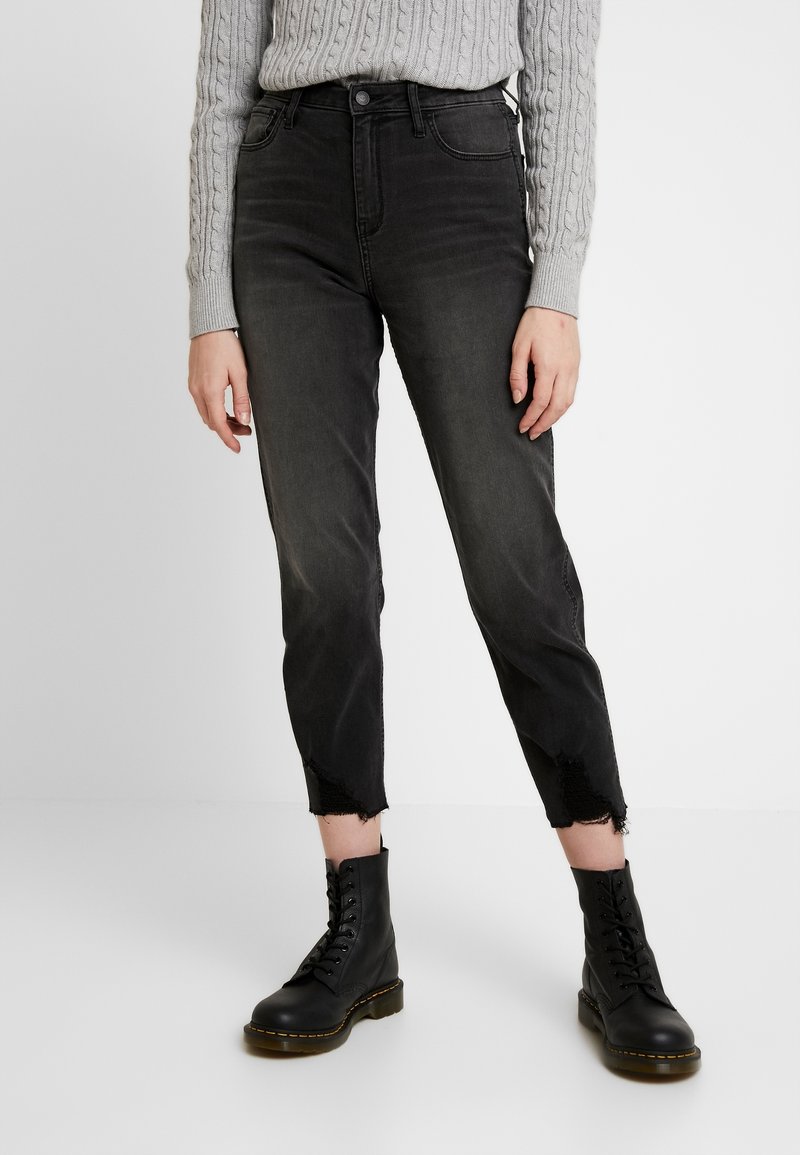 High-waisted black denim jeans featuring a tapered leg, frayed hems, and subtle fading, paired with black lace-up ankle boots.