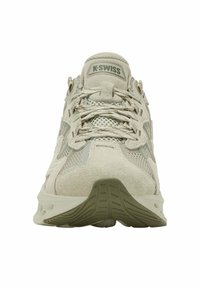Beige K-Swiss kengät, joissa on verkko- ja mokkanahka-yksityiskohtia, paksu pohja ja ristikkäin narut, esitetty etuviistosta valkoista taustaa vasten.