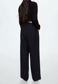 Haut en maille noire à manches longues, associé à un pantalon à pinces à taille haute, jambes larges, à rayures fines, avec poches et texture lisse.