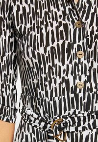 Zwart-witte gestreepte jurk met een knoopsluiting aan de voorkant, korte mouwen, een ceintuur in de taille en een gouden gespsluiting.