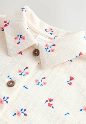 Košulja od kremasto teksturiranog tkanina s ovratnikom, ukrašena malenim crvenim i ružičastim cvjetnim uzorkom te smeđim gumbima.