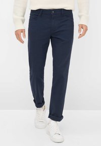 Marineblauwe katoenen broek met een rechte pijpdesign, voorzien van opgerolde manchetten, een voorkantzak en een enkele knoopsluiting. Gecombineerd met witte sneakers.