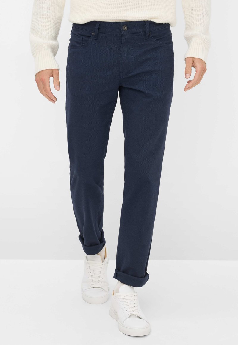 Marineblauwe katoenen broek met een rechte pijpdesign, voorzien van opgerolde manchetten, een voorkantzak en een enkele knoopsluiting. Gecombineerd met witte sneakers.