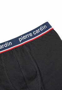 Zwarte onderbroek met een marineblauwe elastische tailleband waarop in witte letters "pierre cardin" staat, aangevuld met rode en witte strepen. Gladde textuur.