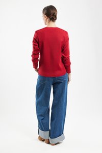 Czerwony sweter z okrągłym dekoltem, ściągaczami przy mankietach i u dołu. W połączeniu z jasnoniebieskimi, szerokimi spodniami dżinsowymi z podwiniętymi mankietami.