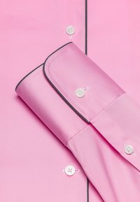 Camicia da uomo rosa con texture liscia, colletto button-down, bottoni bianchi e piping nero lungo i bordi dei polsini e della patta.