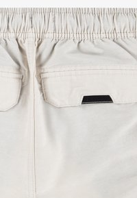 Ljusbeiga shorts med elastisk midja, två bakfickor och en svart detaljer på fickklaffen. Slem ytstruktur.