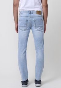 Jeans de mezclilla azul claro con un corte recto, que cuentan con una etiqueta de cuero en la parte trasera y dos bolsillos traseros con costuras en contraste.