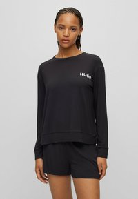 Zwarte lange mouw shirt van gladde stof, met een ronde halslijn en het "HUGO" logo in het wit op de linker borst. Gecombineerd met bijpassende shorts.